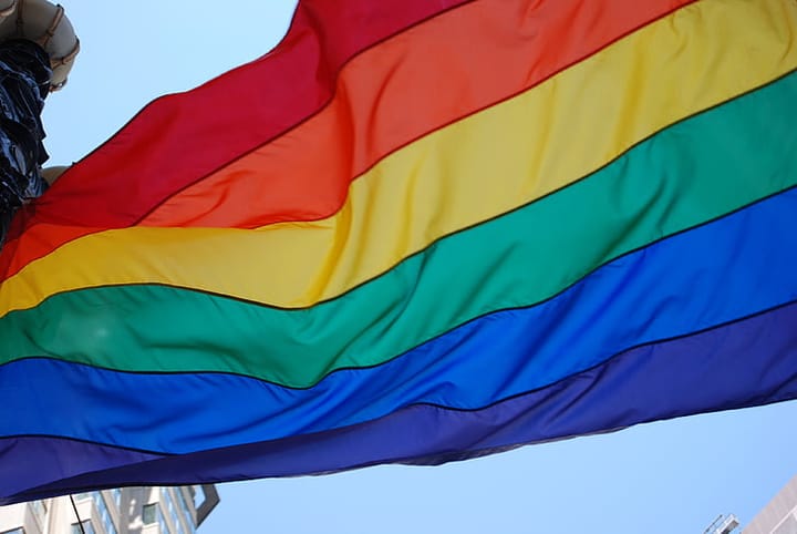 A picture of a pride flag flying in front of a blue sky.